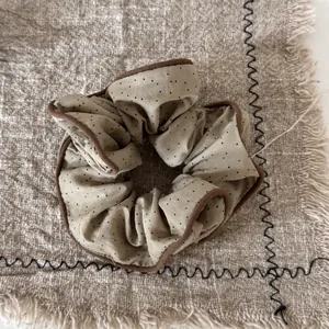 Close-up detail of a beige polka dot pleated scrunchie hair tie with brown piping edge