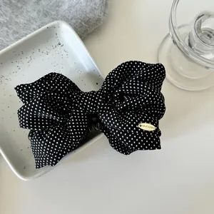 Close-up of black polka dot bow hair clip with gold YAFANNI brand tag on white tray