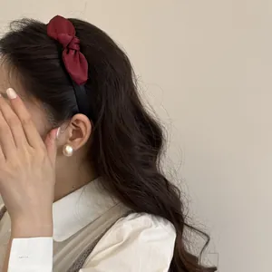 Close-up view of an elegant red satin bow headband worn by a model with a pearl earring.
