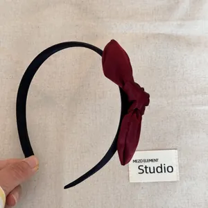 Detailed view of an elegant burgundy satin bow headband on a neutral linen backdrop