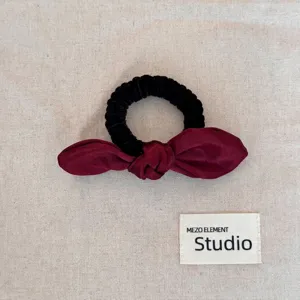 Detail showing the burgundy satin bow hair scrunchie and black ribbed elastic band