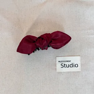 Close-up view of a deep burgundy satin bow hair clip resting on a neutral beige canvas.