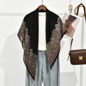 Élégante écharpe en mousseline noire avec bordure paisley, présentée sur un cintre