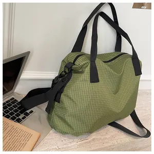 Large capacity green checkered nylon tote bag with black shoulder straps on a desk next to a laptop