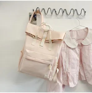 Detailed side view of a light pink casual roll-top backpack hanging on a metal wall hook