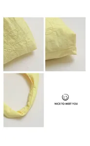 Macro view of yellow nylon tote bag details featuring floral embroidery and crinkled texture.