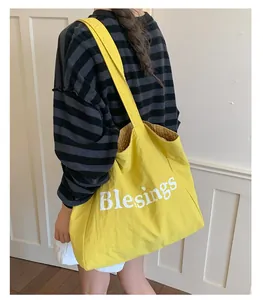 Detailed view of large yellow canvas tote bag with white letters and plaid lining.