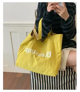 Detailed view of yellow nylon tote bag with white Blessings print and plaid lining