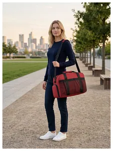 Détail d'un grand sac de voyage rouge porté par un mannequin dans un cadre extérieur.