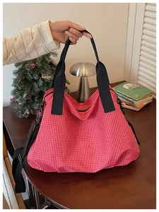 Detail of a large red checkered nylon tote bag held by hand in a cozy lifestyle setting