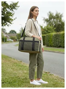 Femme portant un grand sac de voyage vert olive sur son épaule dans un cadre extérieur.
