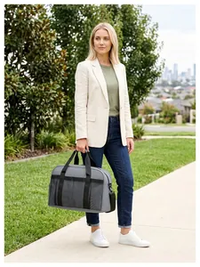 Sac de voyage gris élégant à grande capacité tenu par une femme en tenue décontractée.