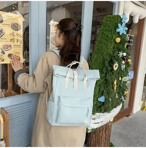 Minimalist light blue roll-top backpack carried by a woman in a stylish urban cafe setting