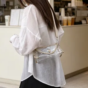 Detailed view of a transparent PVC crossbody bag with gold chain trim worn by a model