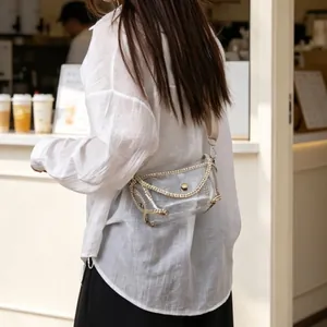 Detail of transparent PVC crossbody bag with gold chain trim worn by a model