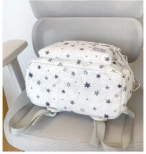 Detailed view of white backpack featuring purple star print and front pocket on a grey chair