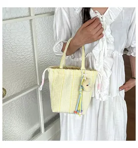 Detalle del bolso de rayas amarillas con cordón y colgante de luna sostenido por modelo