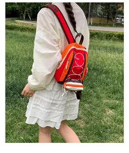 Mochila de montaña roja y naranja llevada por una modelo en un campo de césped.