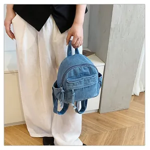 Detailed macro view of a blue denim mini backpack held against stylish white trousers