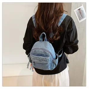 Rear view of a stylish blue denim mini backpack worn by a model in a casual setting