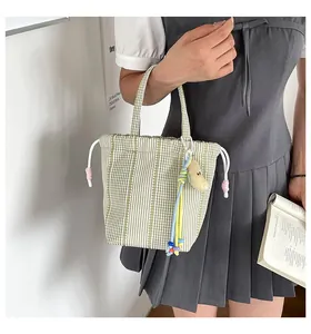 Detalle de un bolso de cuadros vichy verdes con un colgante pequeño y adorable.