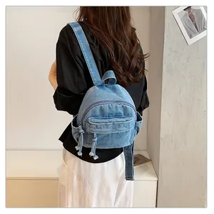 Back view of a stylish blue denim backpack on a woman in a minimalist indoor room