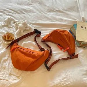 Coppia di borse a tracolla arancioni in nylon a forma di mezzaluna su un morbido letto bianco