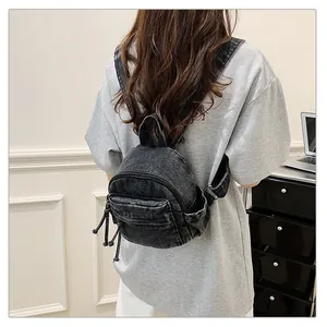 Close-up back view of a mini washed denim backpack worn by a model for a casual look