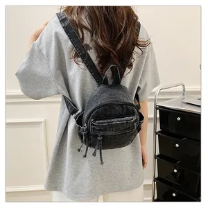 Back view of a casual black denim mini backpack worn by a female model in grey t-shirt