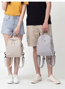 Modelli con mini zaini impermeabili beige e grigi, che mostrano le dimensioni da viaggio.