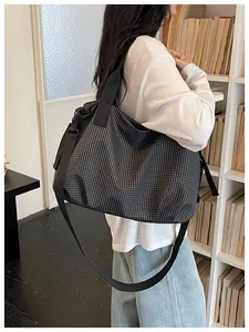 Large capacity checkered nylon tote bag shown carried by a model in a library setting.