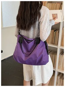 Side view detail of a purple checkered tote bag with black straps carried by a model.
