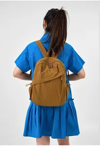 Detailed back view of a minimalist brown nylon backpack worn by a model in a bright blue dress