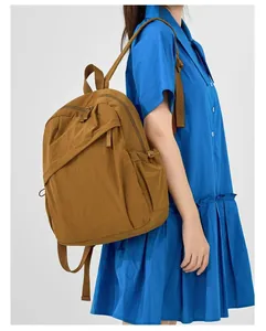 Side view of a brown nylon commuter backpack worn by a model in a blue dress.