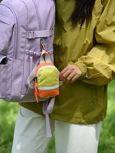 Colorful mini backpack pouch charm hanging on a purple rucksack in outdoor setting