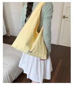 Detailed view of a light yellow nylon tote bag with floral embroidery worn by a model