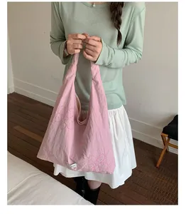 Model holding a pink nylon tote bag featuring delicate embroidered floral patterns
