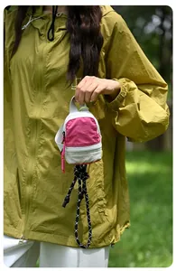Close-up of a pink mini storage pouch with a braided lanyard held by hand outdoors