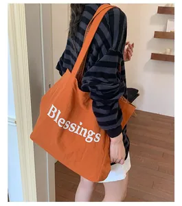 Woman wearing a large orange nylon tote bag with "Blessings" print in a cozy room.