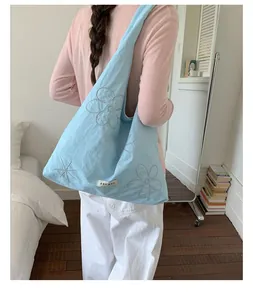 Back view of model carrying light blue floral nylon tote bag in a casual room setting