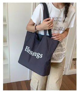 Detailed shot of a large black nylon tote bag with 'Blessings' text and plaid lining