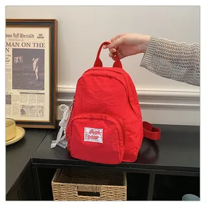 Close-up of a vibrant red nylon backpack held by hand in a cozy room setting