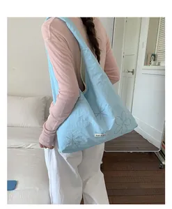 Back view of a model wearing a light blue nylon tote bag with floral embroidery detail