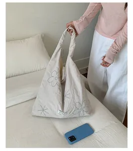 Large cream nylon tote bag with embroidered floral details shown in a lifestyle bedroom setting
