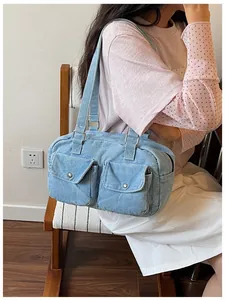 Detail view of light blue denim Boston bag with front pockets carried by a model.