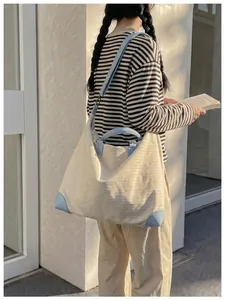 Modella con una grande borsa da viaggio beige e azzurra in un ambiente casual.