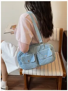 Detailed view of a light blue large capacity denim shoulder bag worn by a model sitting.