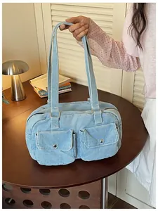 Close-up of a large light blue denim Boston bag with two front flap pockets and straps