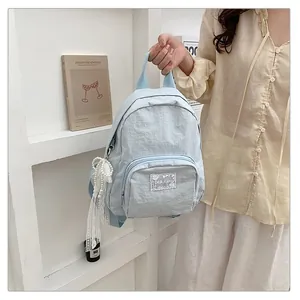 Detail view of a light blue student backpack with a pearl and lace charm