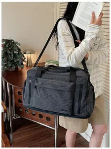 Large checkered travel duffel bag held by a model in a cozy lifestyle indoor setting